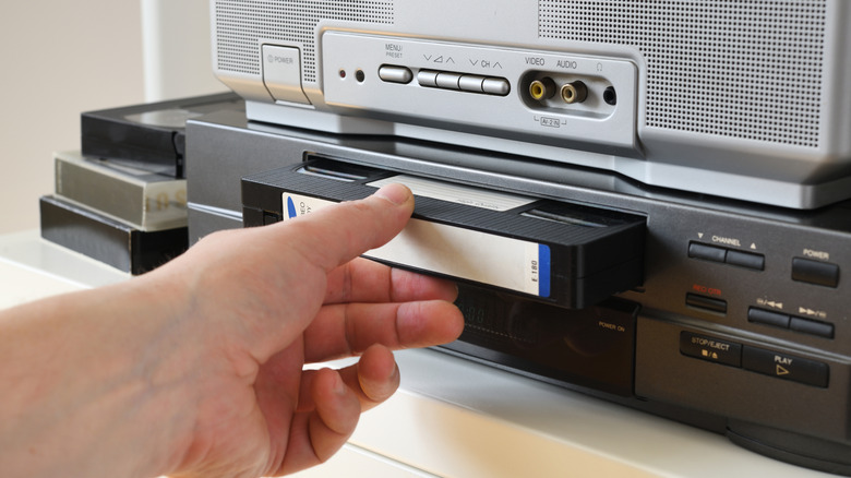 Hand inserting a VHS tape into a video cassette player at home