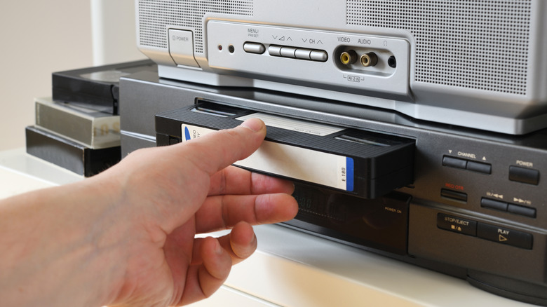 Hand inserting a VHS tape into a video cassette player at home