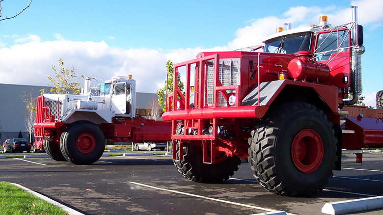 Two Kenworth 963 trucks in a parking lot, front 3/4 view