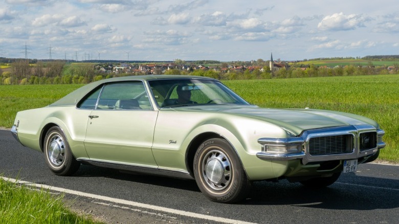Green 1969 Oldsmobile Toronado driving on a country road