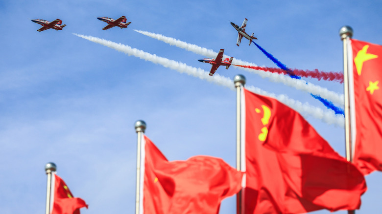 Fighter aircraft flying in the air with Chinese flags in the foreground.