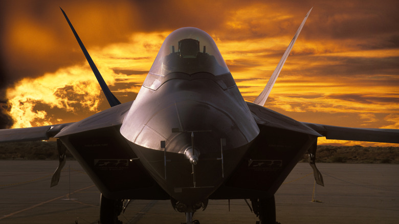 An F-22 Raptor parked on a runway with a sunset in the background