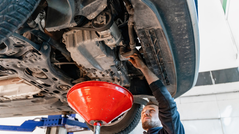 Mechanic performing oil change with drain funnel beneath car on lift