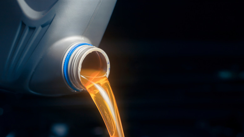 Bright straw-colored oil being poured out of bottle, isolated on black background