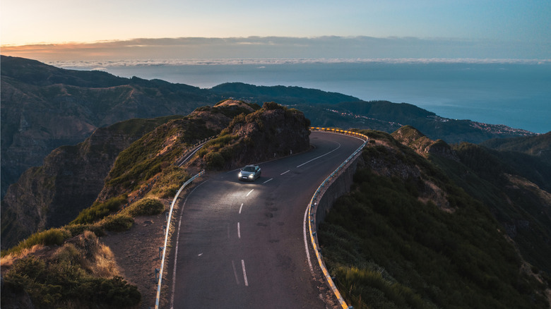 An image of a car driving on a mountain pass with sunset in the background.