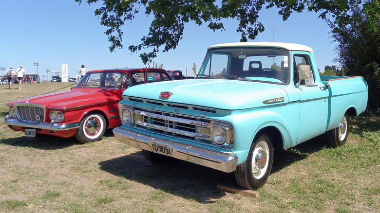 1961 Ford F-100 pickup truck parked beside another vintage vehicle under a tree
