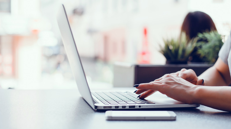 woman with black nails typing on a laptop keyboard