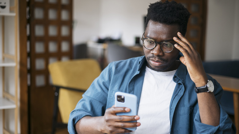 person with glasses frowning at smartphone