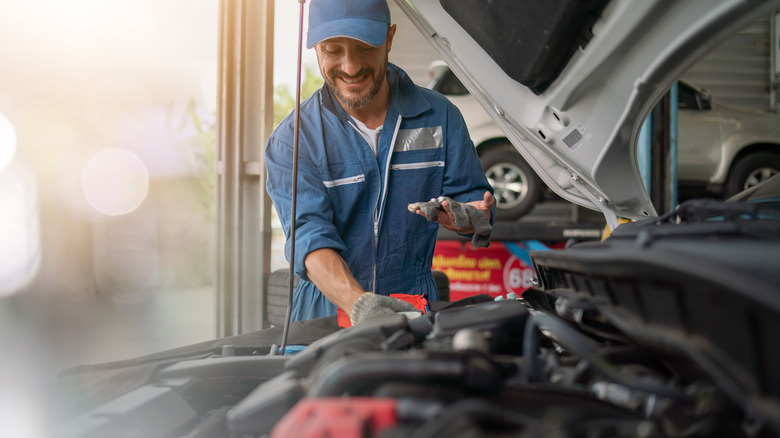 A smiling mechanic next to a car with the hood raised