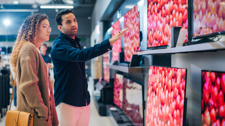 A man and a woman looking at TVs for sale inside a retail space