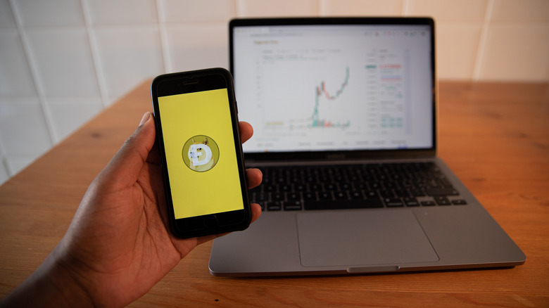 Dogecoin on cellphone in front of laptop