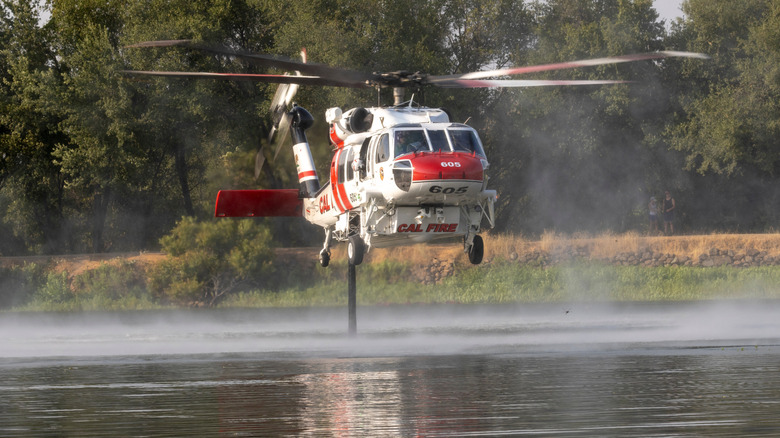 A Sikorsky S-70 "Firehawk" helicopter pumping water out of a small body of water