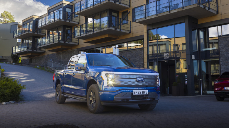 A blue Ford F-150 Lightning outside a modern building, front 3/4 view, UK plates