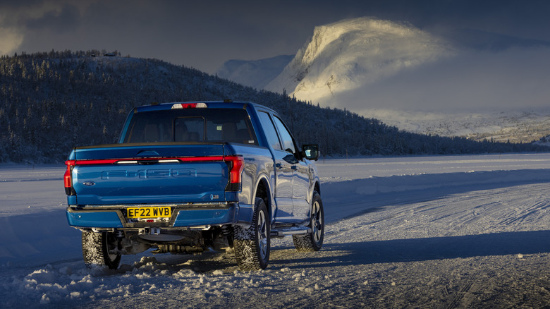 Rear 3/4 view of a blue Ford F-150 Lightning in the snow, UK license plates