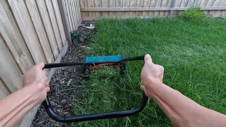 A man trying to cut long grass with a cylinder mower