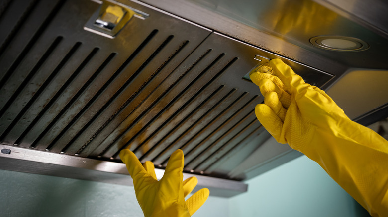 A person wearing gloves and opening a kitchen range hood.