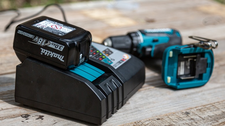 A Makita battery on a charger beside a drill.