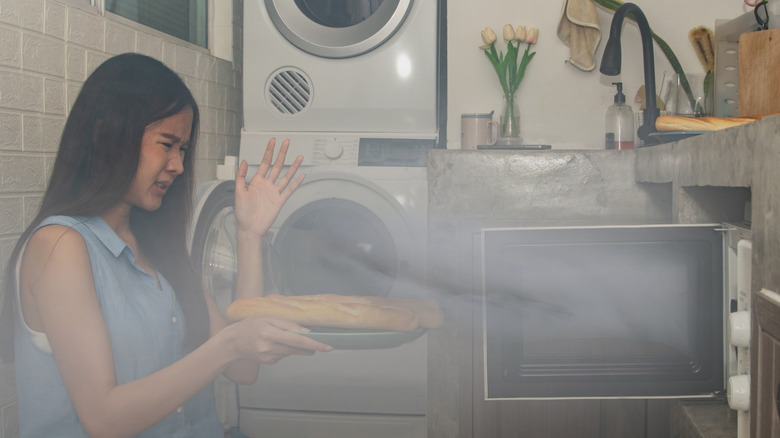 A lady holding bread and the microwave seems to be broken