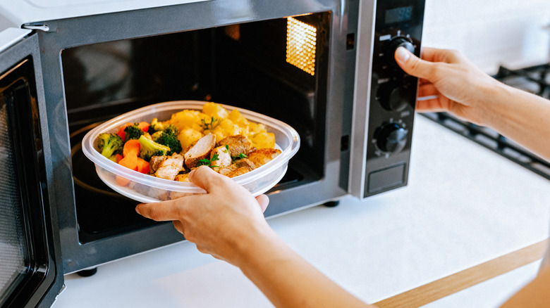 A ladies hand placing colorful food in a microwave