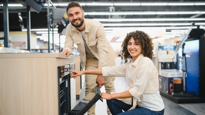 A smiling couple looking at an oven in a store selling appliances