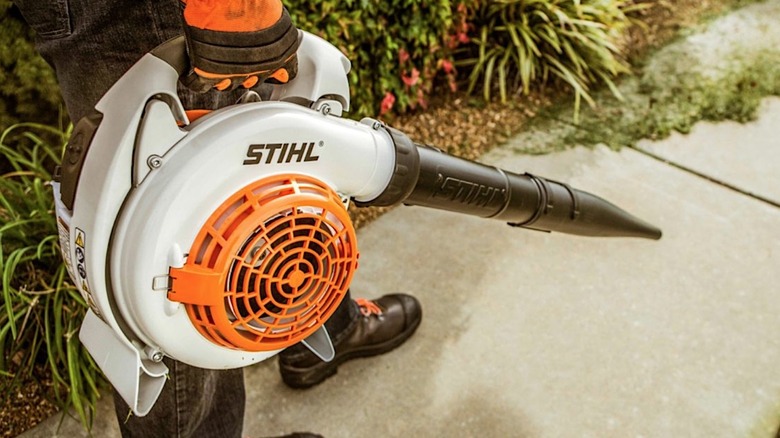 Waist-down photo of person holding Stihl leaf blower over sidewalk