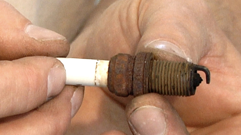 A close-up of a mechanic holding a rusted spark plug