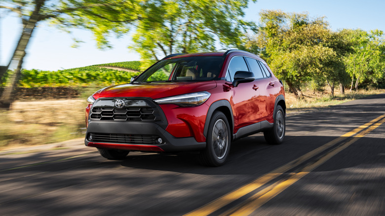 Front 3/4 view of the Toyota Corolla Cross in Soul Red Crystal on a countryside road