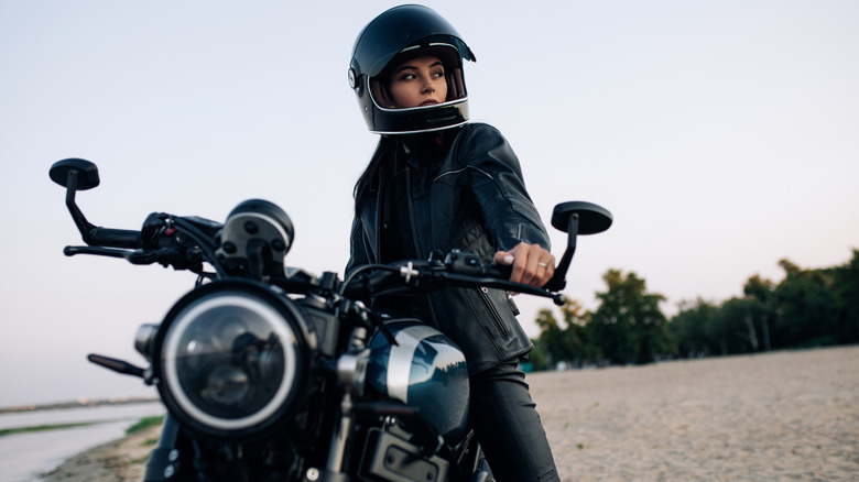 Young woman sits on black motorbike in helmet and leather jacket