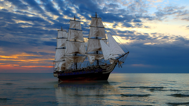 Old 18th century ship on calm ocean water at sunset