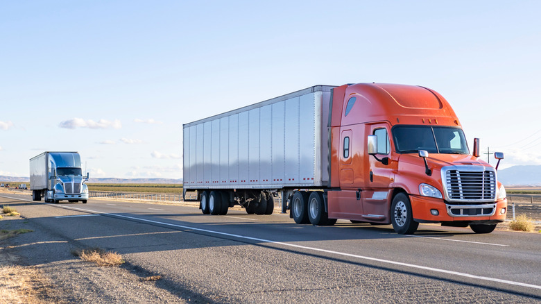 Two semi-trailer trucks on a highway, front 3/4 view