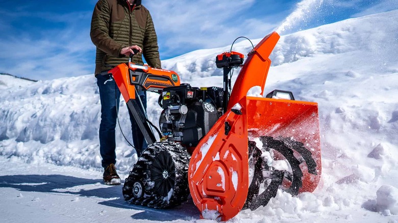 An Ariens two-stage snow blower being used to clear a snowy driveway