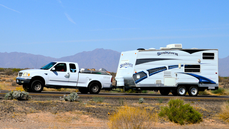 An older Ford F-150 towing a camper trailer in the desert