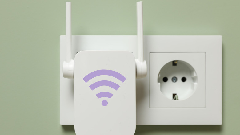 New modern repeater with Wi-Fi symbol plugged into socket on light green wall
