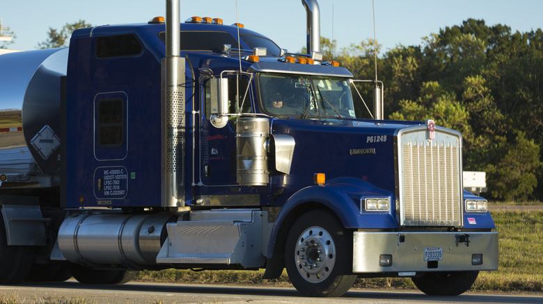 Vista frontal de 3/4 cuartos de un camión Kenworth de eje azul, con un petrolero adjunto