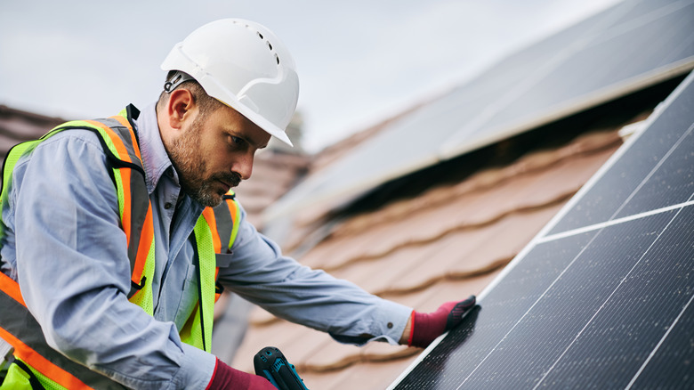 A man in a hard hat installing a solar panel on a brown roof