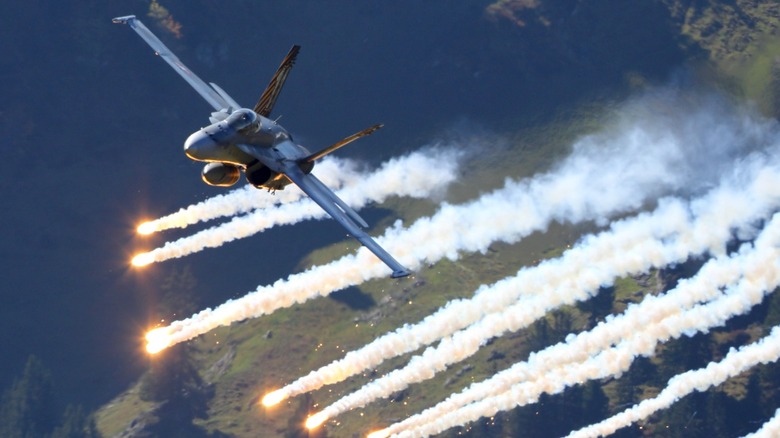 An F/A-18 fighter jet in flight releasing chaff and flare behind it