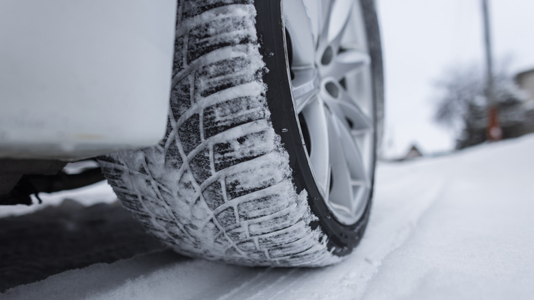 Close-up of a snow-covered tire on a snowy road.