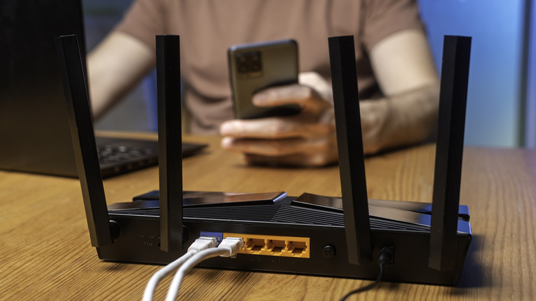 Close-up of a Wi-Fi router on a desk with a man in the background using a laptop and smartphone