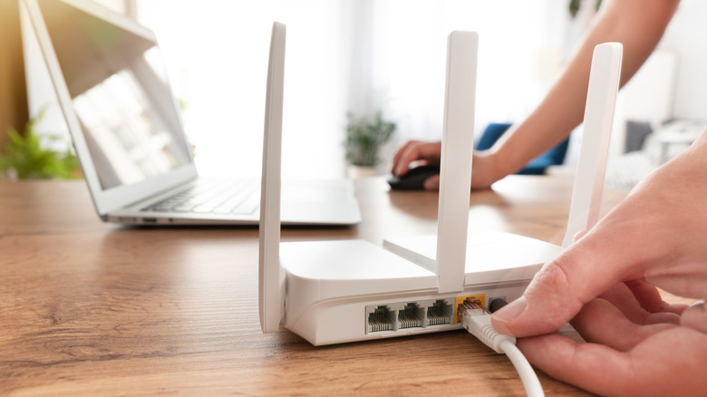 A person plugging in an Ethernet cable to a router on a desk