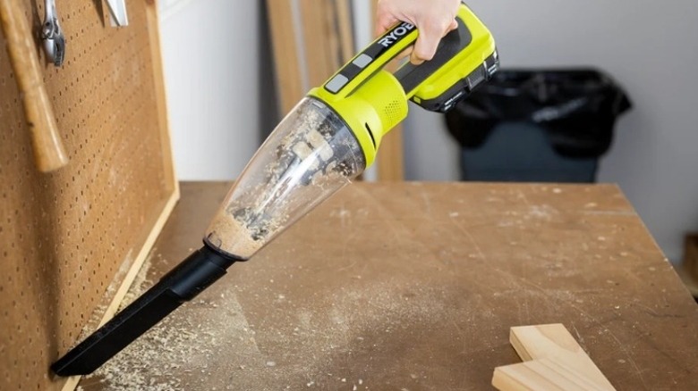 Green and black handheld vacuum cleaning sawdust from a workspace