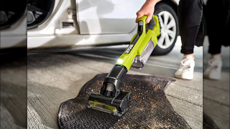 Green and black handheld vacuum cleaning a car floor mat