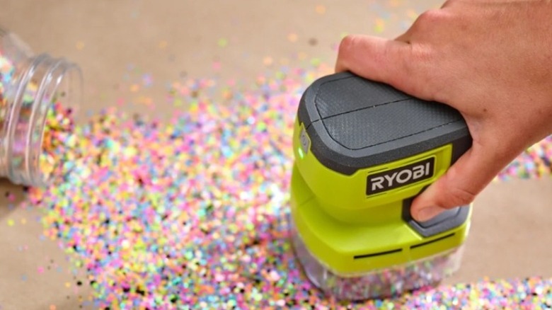 Small green hand vacuum cleaning spilled glitter