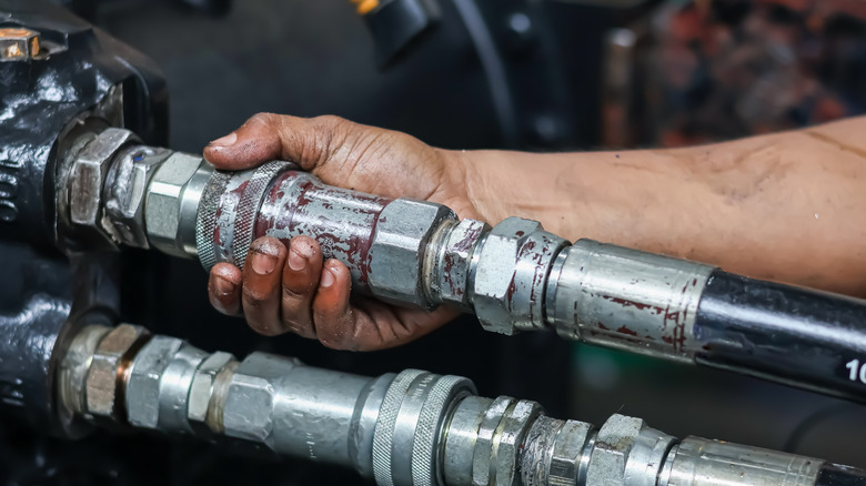 Close-up of person's hand holding high-pressure hydraulic line connector
