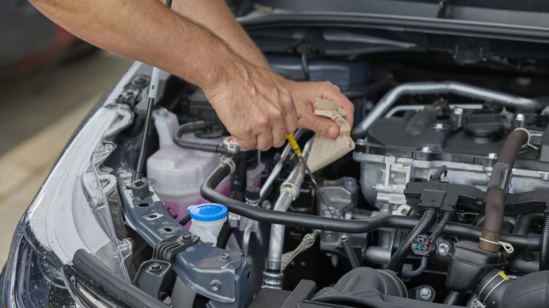 Man using a dipstick to check engine oil level in hybrid car