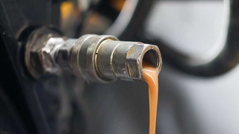 Close-up of milky contaminated hydraulic oil emerging from nozzle