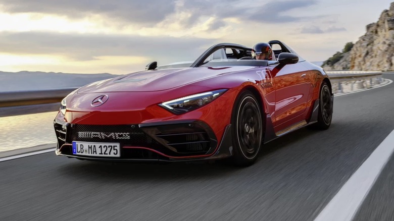 A red AMG converitible driving fast with a cliff on one side and a lake on the other. The driver is wearing a helmet.