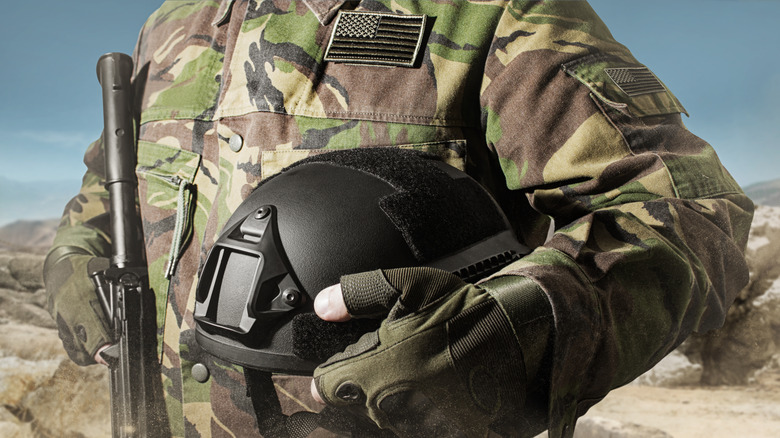 Photo of an unknown solider holding a gun and military-spec helmet and gear.
