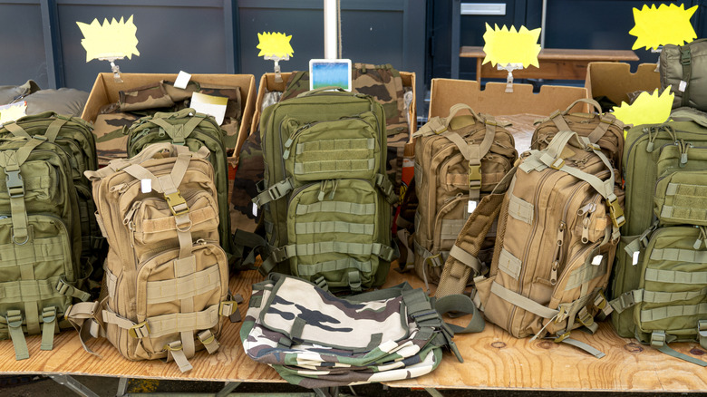 A group of military-grade backpacks sitting on a bench for sale.