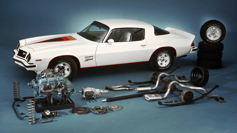 A 1977 Chevy Camaro displayed behind its engine, drivetrain, and other performance parts