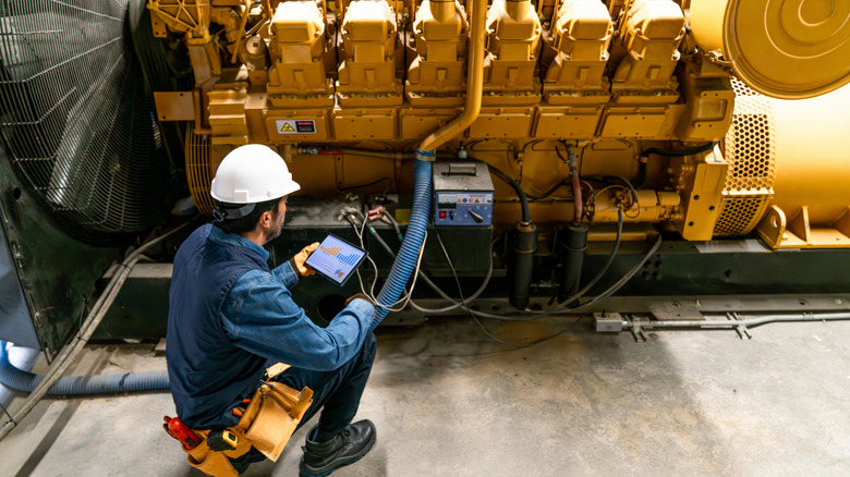 Engineer using a tablet to monitor the performance of a large, static, diesel engine.